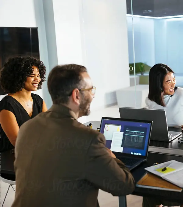 A group of three individuals gathered around a table, focused on a laptop in front of them.